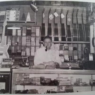 Amos Arthur behind the counter at Arthur’s Music Store in the 1950s, surrounded by instruments, sheet music, and musical accessories.