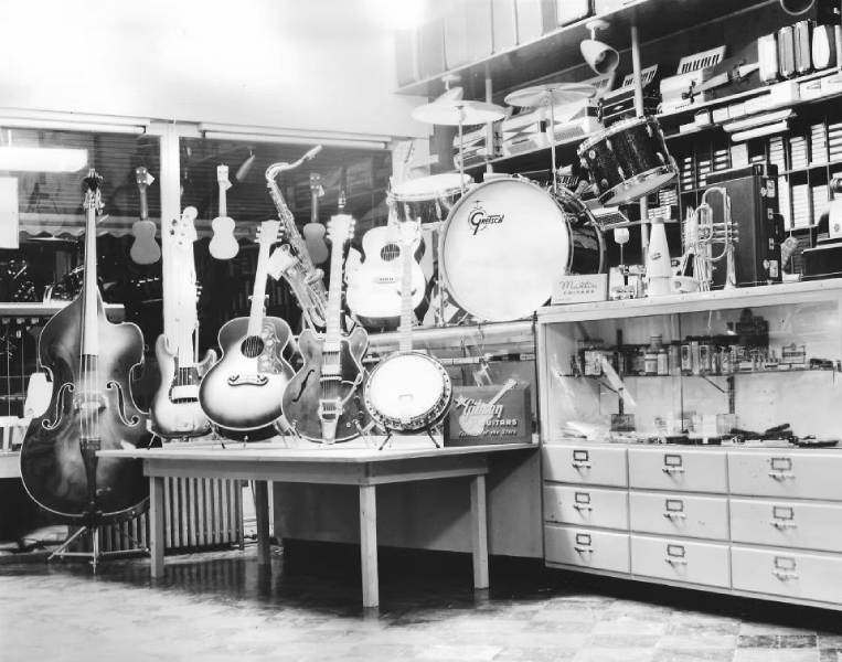 Inside Arthur’s Music Store in 1958, with guitars, an upright bass, a banjo, drums, accordions, and wind instruments filling the displays.
