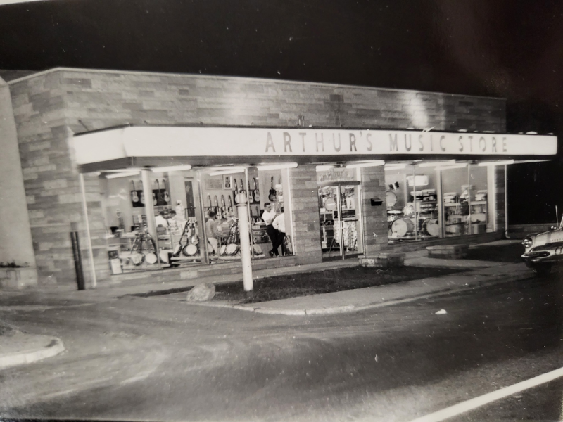 A nighttime view of Arthur’s Music Store at 931 Shelby Street in Indianapolis, likely from the late 1950s or 1960s, with illuminated display windows showcasing instruments.