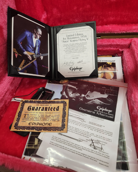 Certificate of authenticity, owner’s manual, and accompanying paperwork for the Epiphone Limited Edition Joe Bonamassa “Amos” 1958 Korina Flying V, displayed in its pink-lined case.