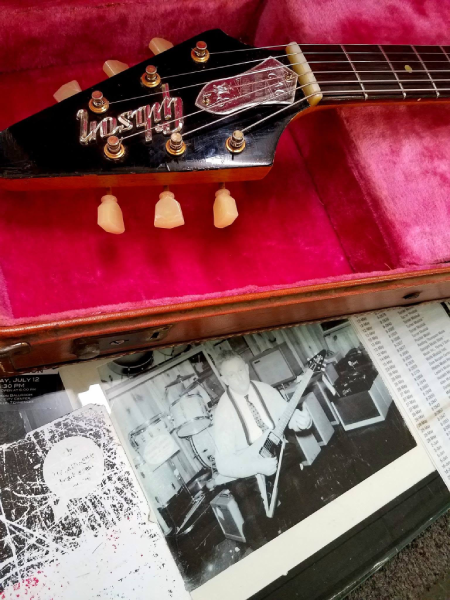 The headstock of the original 1958 Gibson Flying V known as “Amos,” displayed above a photograph of Amos Arthur holding the same guitar in 1958.