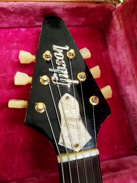 Headstock detail of “Amos,” the original 1958 Gibson Flying V, showing the Gibson logo and decorative truss rod cover bearing Amos Arthur’s name.