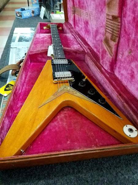 A close view of “Amos,” the original 1958 Gibson Flying V, resting in its pink-lined case, with its distinctive V-shaped body, black pickguard, and gold-colored tailpiece.