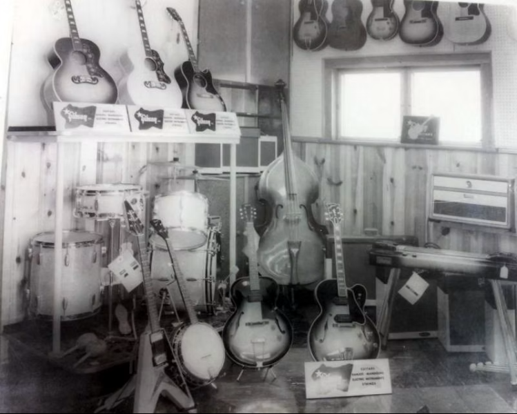 The Gibson Corner at Arthur’s Music Store, circa 1958, with the Flying V displayed at lower left among guitars, banjos, drums, and an upright bass.